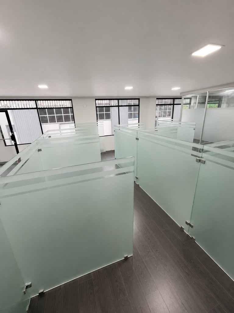 Modern office space with frosted glass partition walls, dark flooring, and bright ceiling lights creating individual cubicles