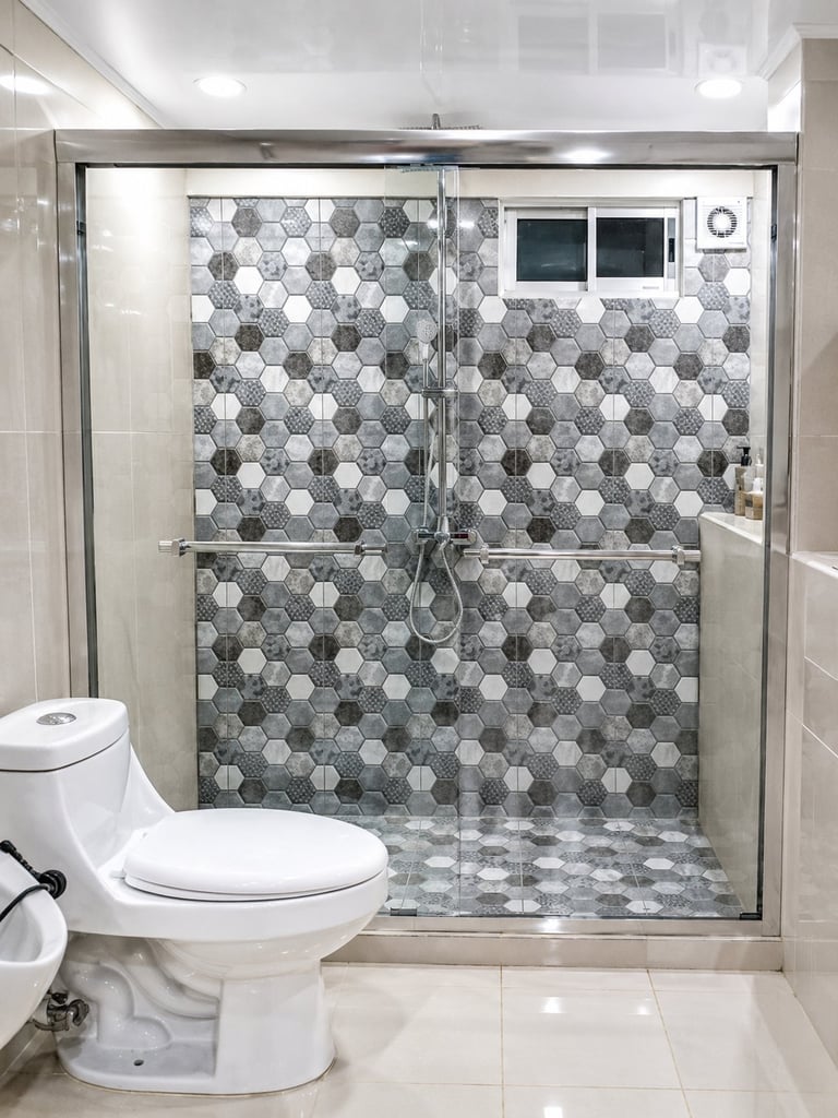 Modern bathroom with glass shower enclosure featuring hexagonal tile backsplash in gray and white tones, white toilet, and polished tile flooring