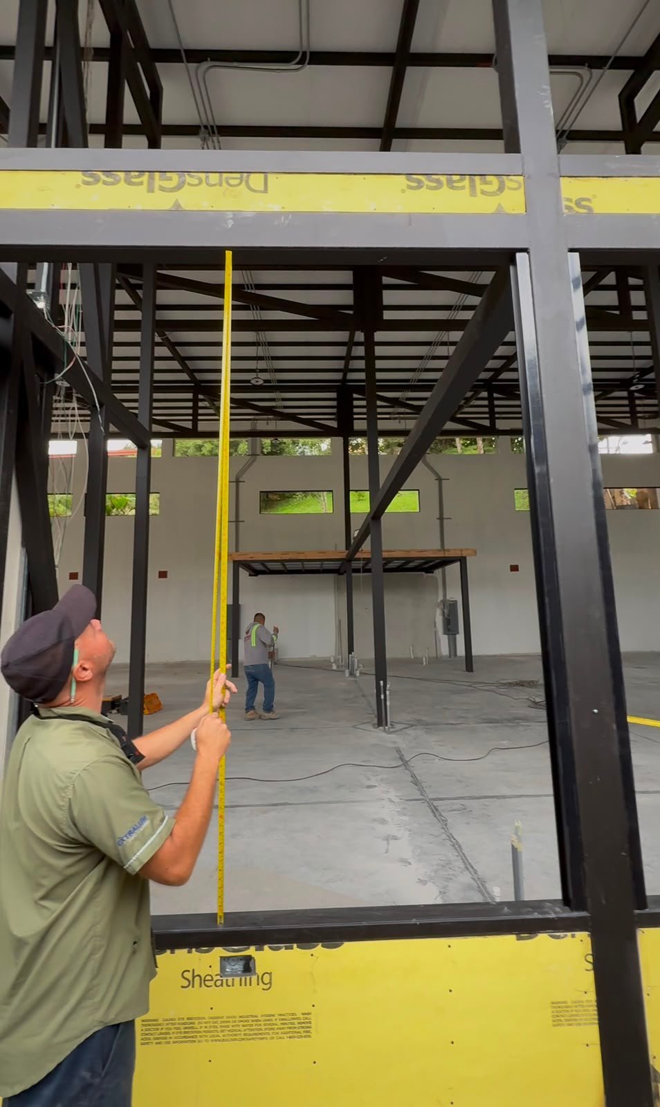 Worker in yellow safety vest holding yellow cable in industrial warehouse under construction with black steel framing