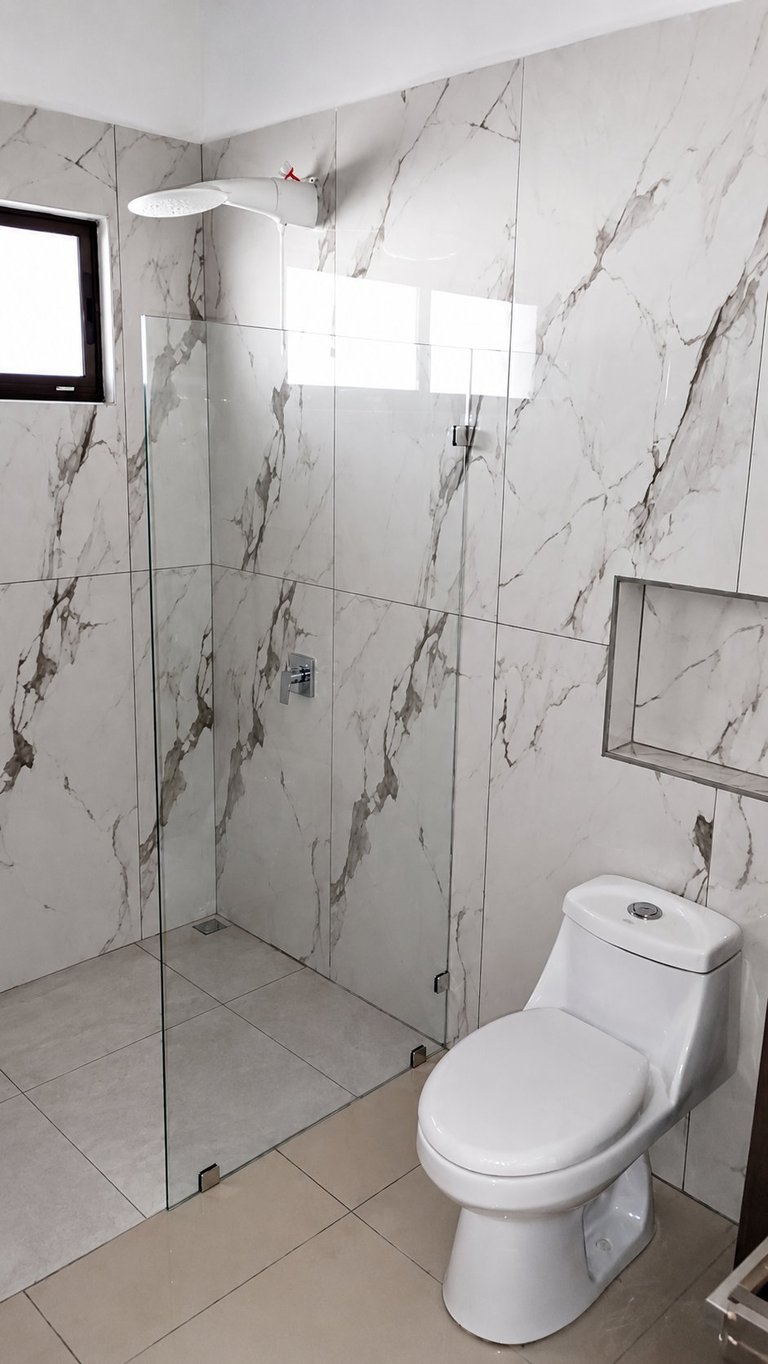 Modern bathroom with marble-patterned walls, glass shower enclosure, white toilet, rainfall showerhead, and small window