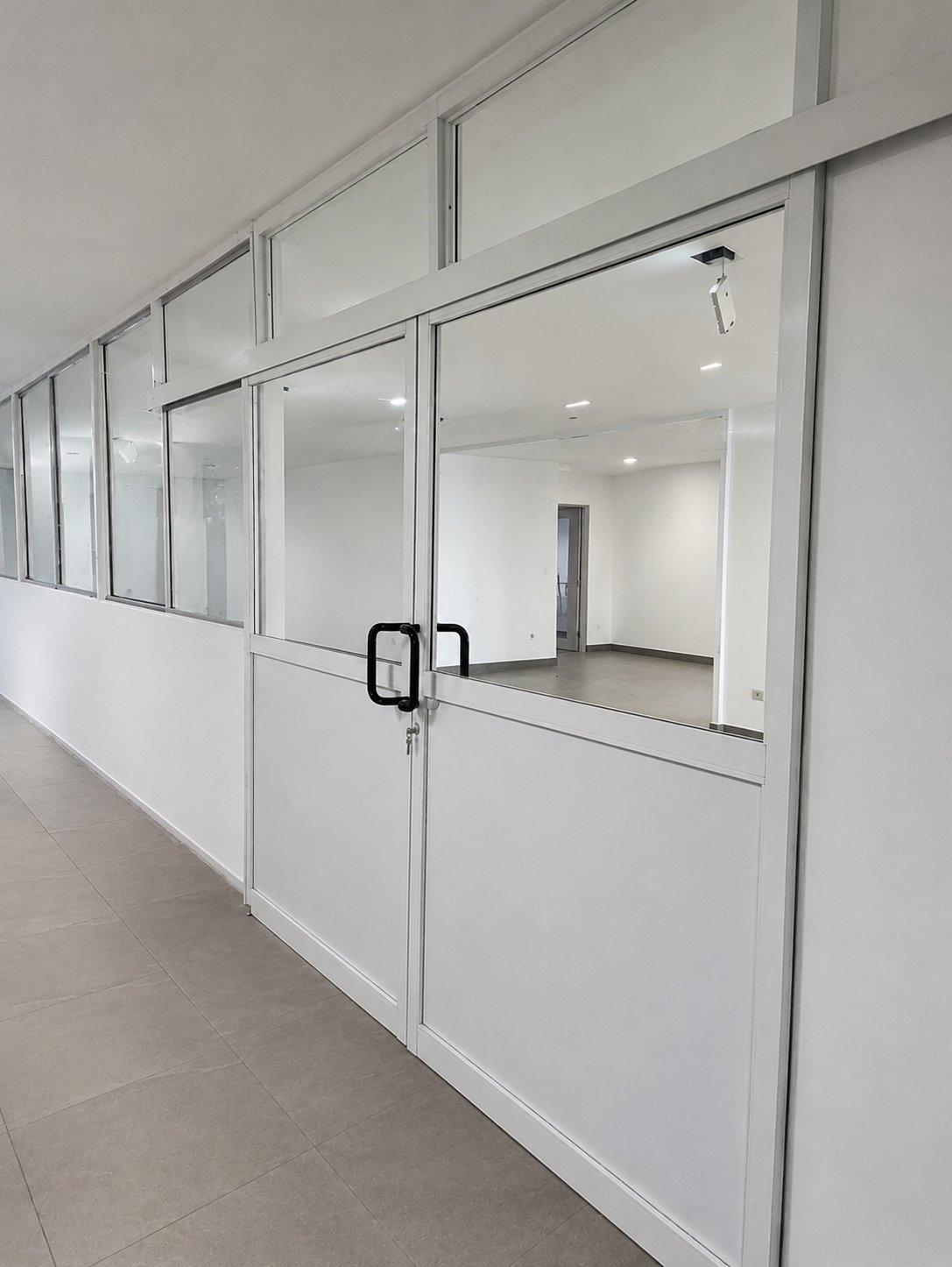 Modern office hallway with white aluminum-framed glass partition walls and doors creating private meeting rooms
