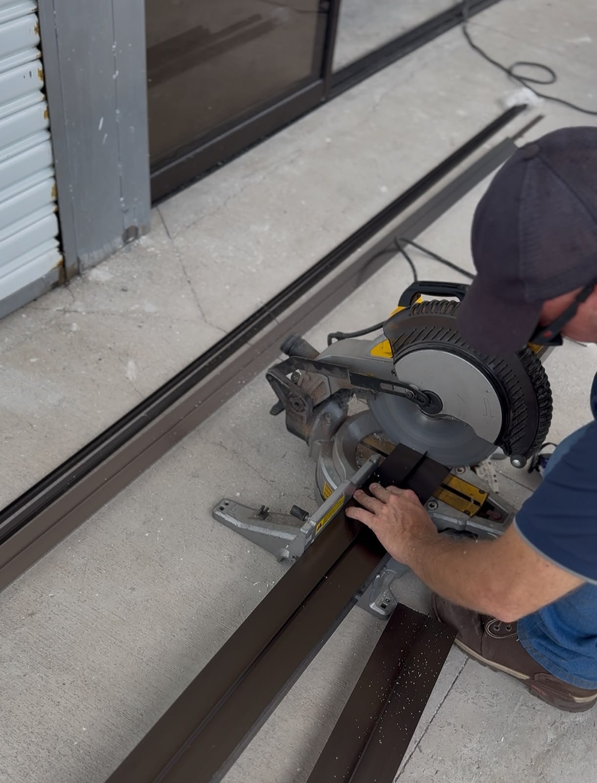 Worker using a miter saw to cut metal trim or threshold on concrete floor near storefront