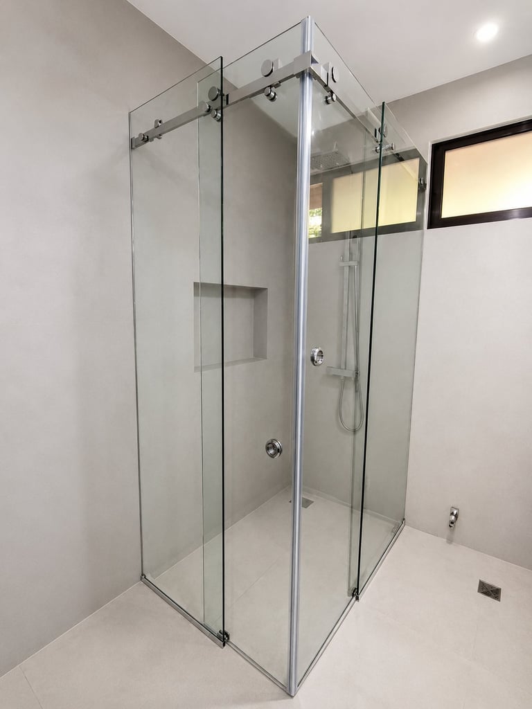 Modern frameless glass shower enclosure with chrome fixtures in a bright bathroom with white walls and tile floor