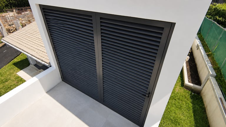 Modern white building exterior with black horizontal louvered doors and surrounding grass and landscaping