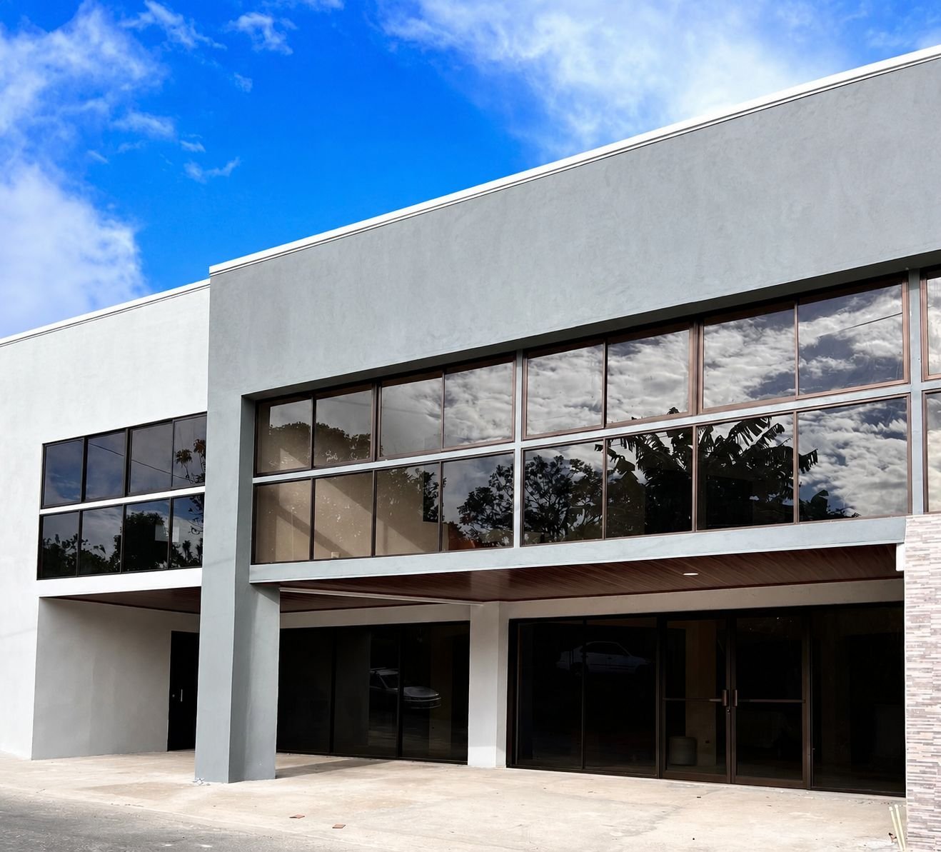Modern white and glass commercial building with large windows and dark entrance doors against blue sky