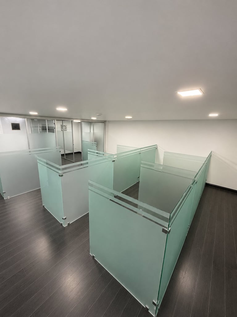 Modern office space with frosted glass partition walls and workstations on dark hardwood flooring under ceiling lights