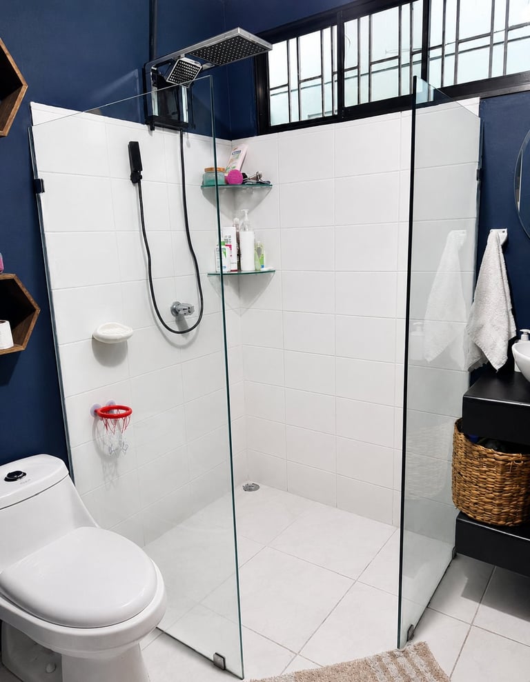 Modern bathroom with white tile shower, glass enclosure, dark blue walls, white toilet, and woven storage basket