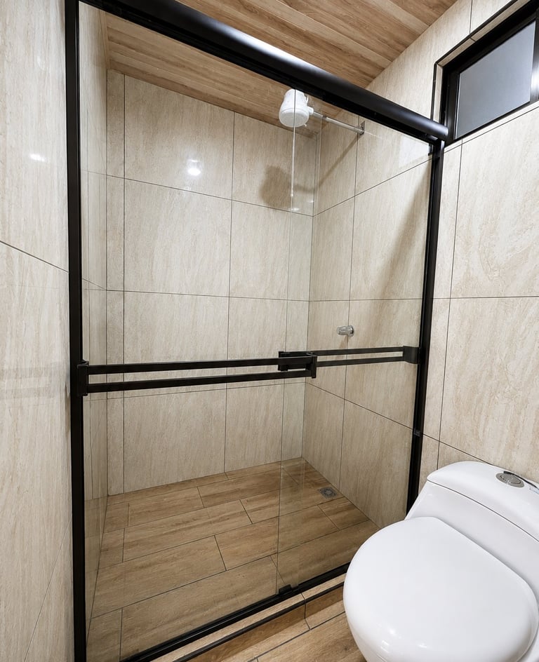 Modern bathroom with glass-enclosed shower, beige tile walls, wooden floor, black framed glass door, and white toilet