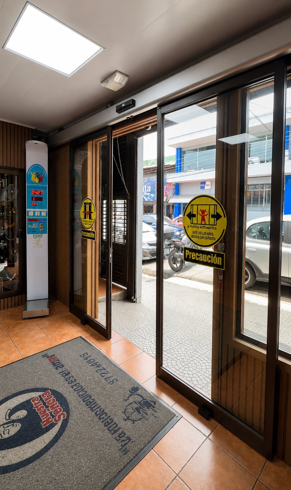 Interior of a commercial auto repair shop entrance with glass doors, yellow caution signs, and a gray welcome mat