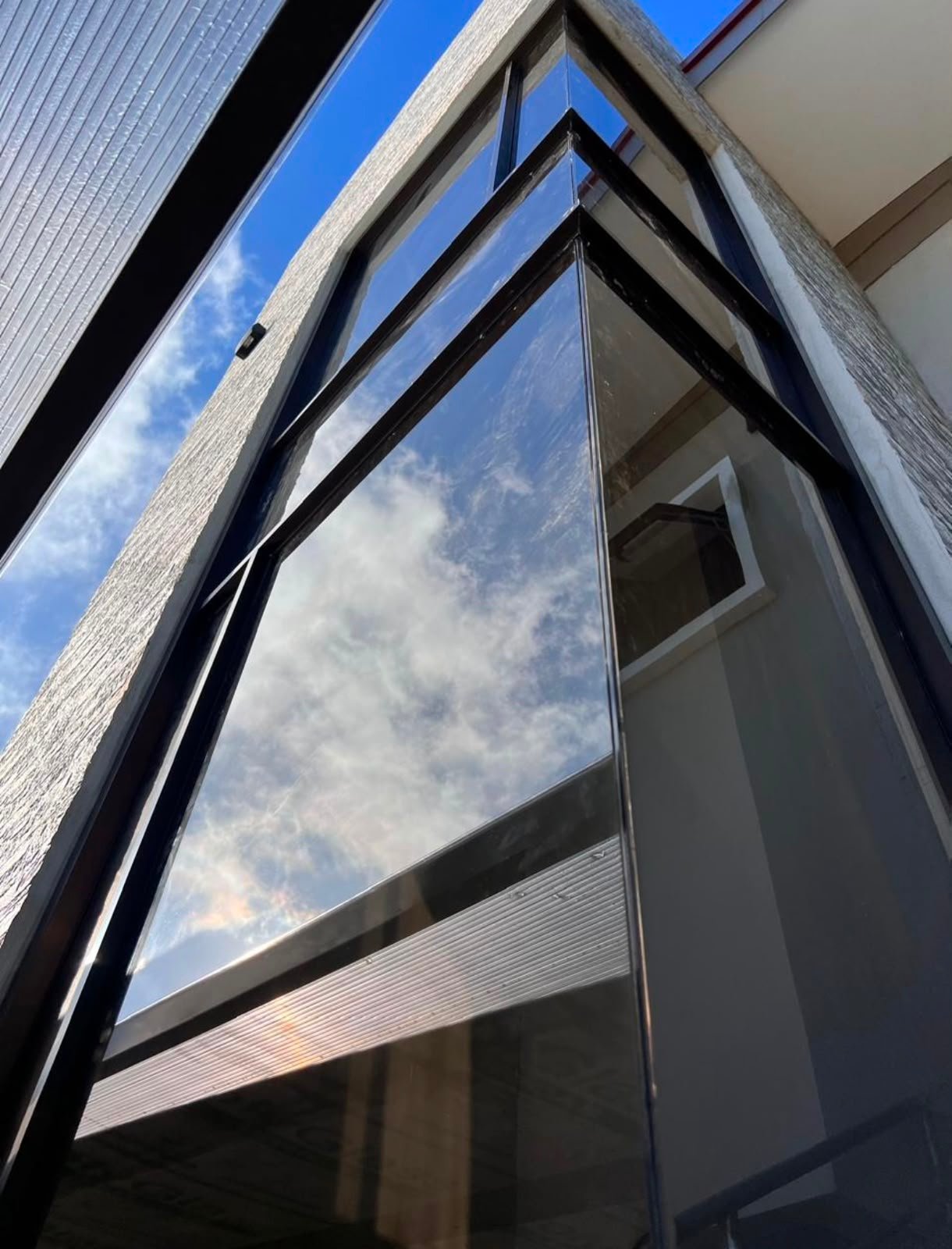 Modern building facade with large black-framed window reflecting blue sky and clouds