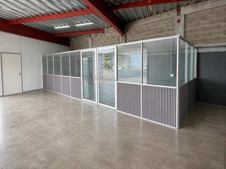 Industrial warehouse space with a large metal-frame glass and aluminum enclosure structure on polished concrete flooring