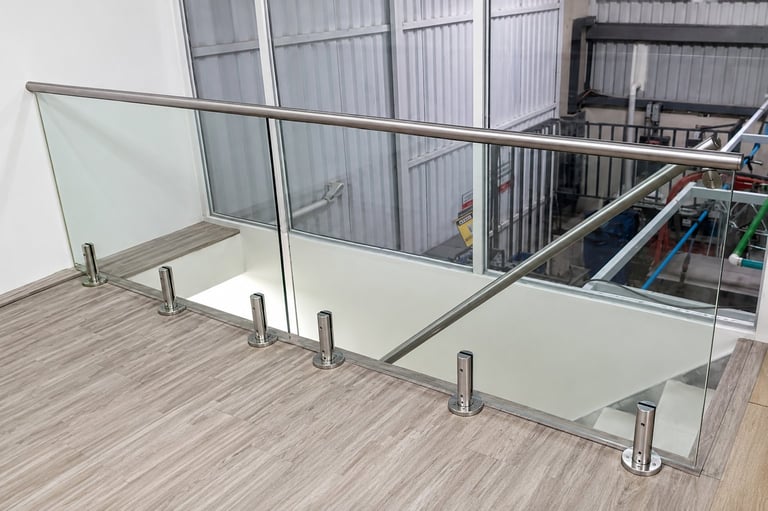 Modern glass railing with stainless steel posts and horizontal cables on a wooden deck overlooking an industrial warehouse space