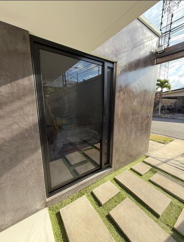 Modern sliding glass door with black frame opening onto a patio with concrete pavers and grass strips
