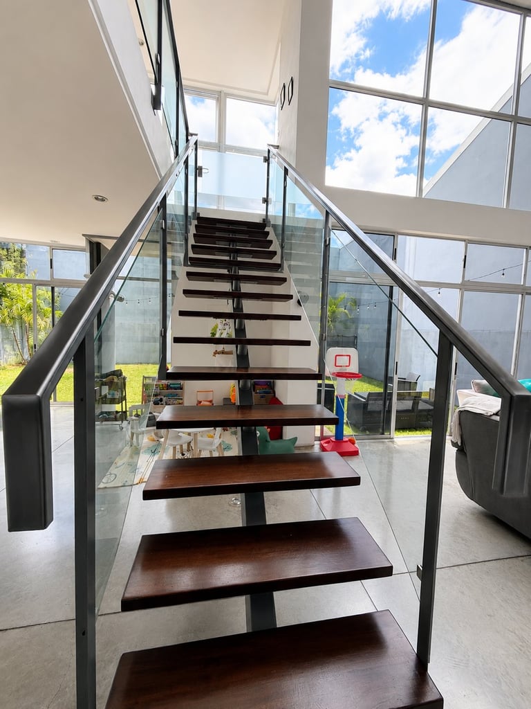 Modern staircase with black metal railings and dark wooden steps leading upward in a bright, minimalist interior with large windows and skylight