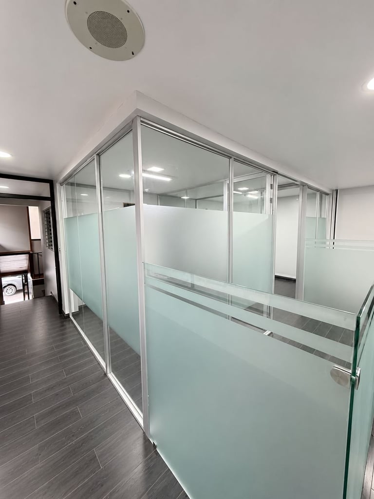 Modern glass-walled office enclosure with frosted panels and aluminum framing in a contemporary workspace with dark wood flooring