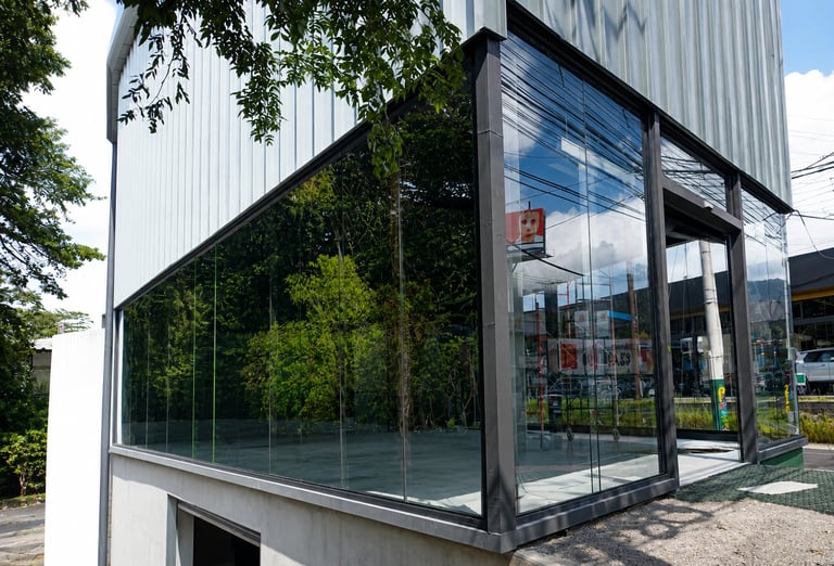 Modern storefront with large glass windows, ivy-covered wall, and corrugated metal exterior on a sunny day