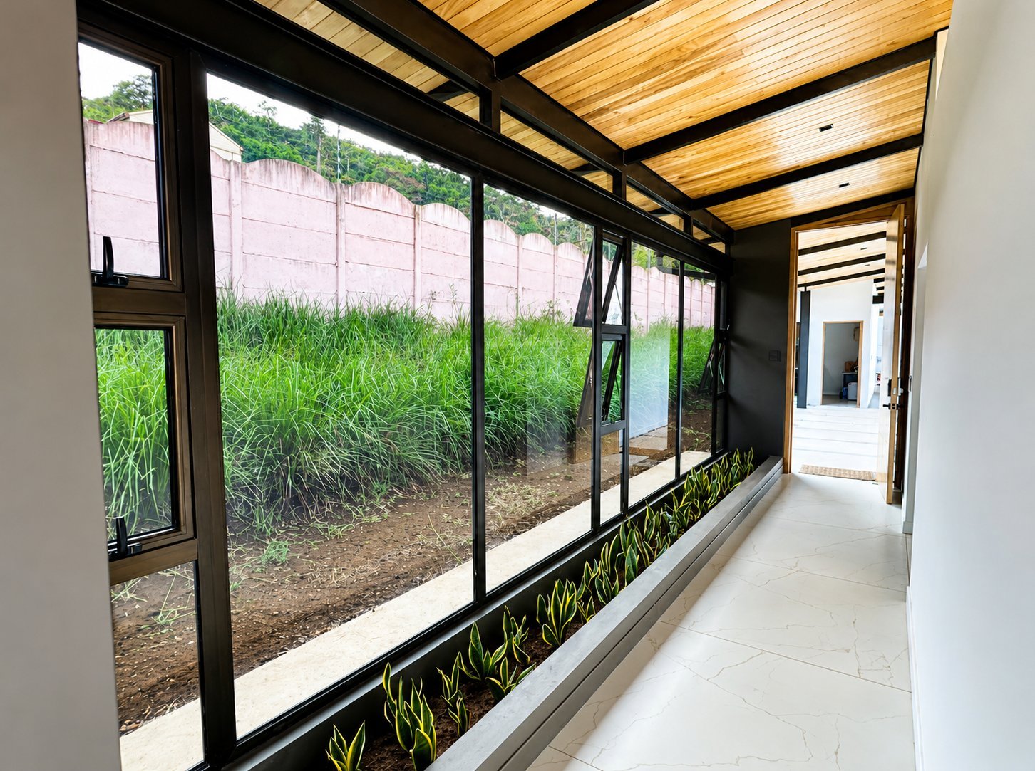 Modern covered walkway with floor-to-ceiling windows overlooking a garden with tall grasses and plants